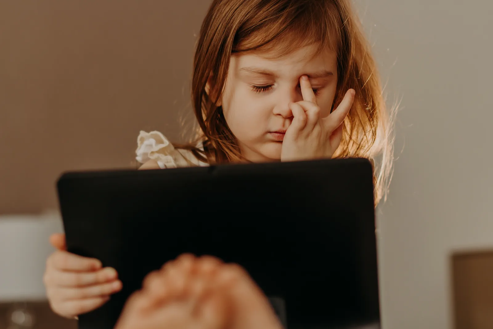 Young girl rubbing her eyes while looking at a tablet